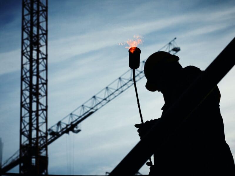 Silhouette of a construction worker with a crane and torch flame in the background. Silhouette of a construction worker with a crane and torch flame in the background.
