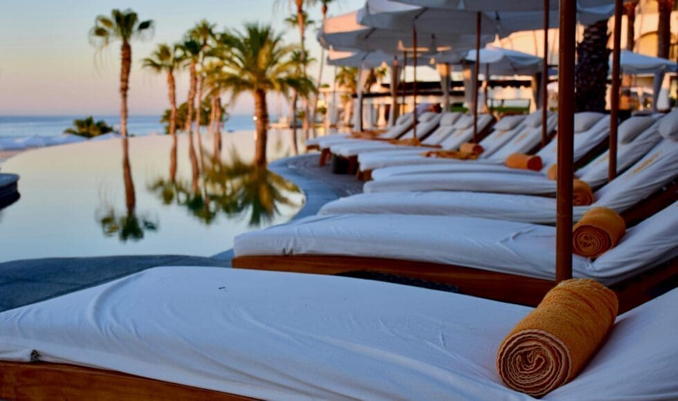 Luxurious poolside lounge chairs with towels at sunset by palm trees.